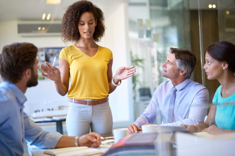 Eine Teamleiterin spricht mit drei Kollegen in einem Büro. Sinnbildlich: Coaching Ausbildung für Führungskräfte und Teamleiter.