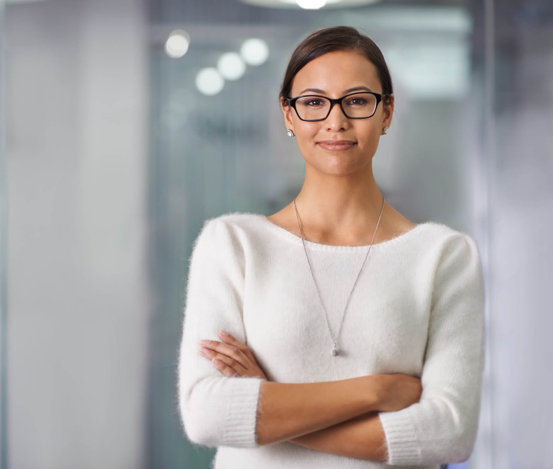 Eine kompetente junge Frau steht mit einer selbstbewussten Haltung vor einer Glaswand im Büro.