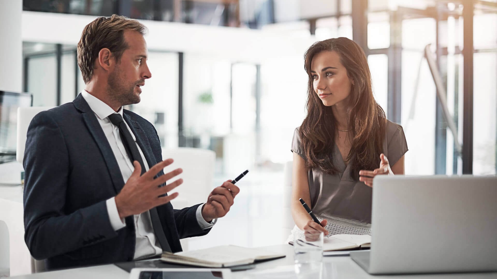 Ein Geschäftsmann und eine Geschäftsfrau laufen einen Gang im Bürogebäude entlang und sprechen während einer Mentoring Session