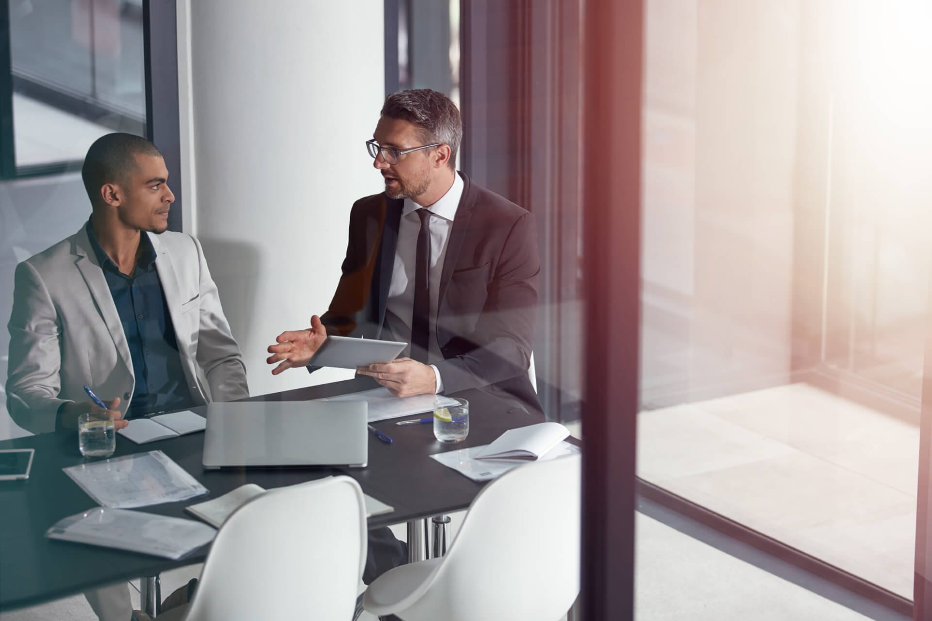 Ein Supervisor spricht mit einem Klienten im Meetingraum und hilft ihm bei der Optimierung seiner Selbstorganisation und Prozesse. Supervision als Instrument zur nachhaltigen Qualitätssicherung.